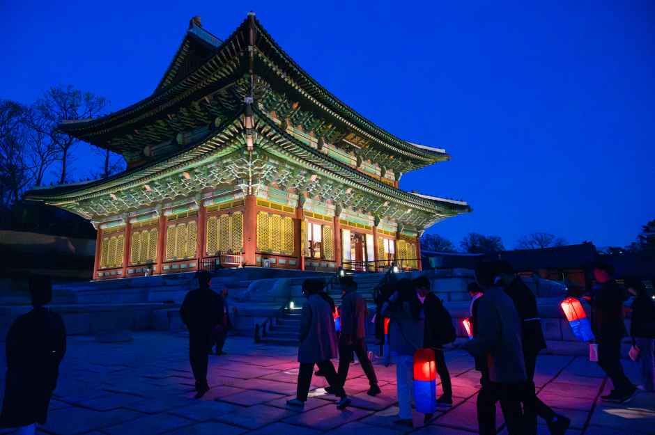 밤에 조명이 켜진 창덕궁 인정전 앞을 청사초롱을 든 관람객들이 걷는 모습