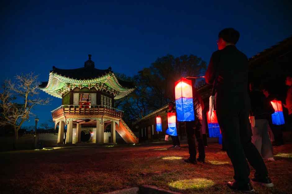 파랑과 빨강 청사초롱을 든 관람객들이 밤의 창덕궁 육각정 앞에 서 있는 모습