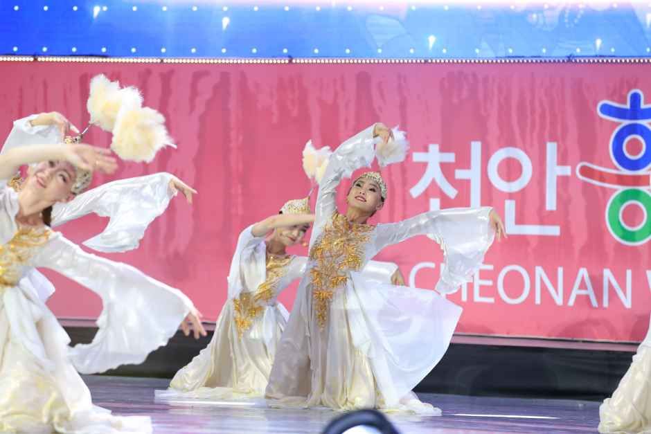 흰색 한복풍 의상을 입은 무용수들이 분홍색 배경막 앞 무대에서 부채를 들고 춤추는 모습