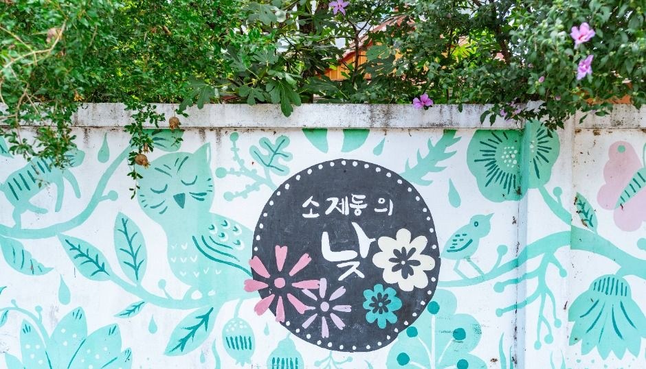 초록 식물이 걸쳐진 담장에 꽃무늬 벽화와 소제동의 낮이라는 글자가 그려진 골목