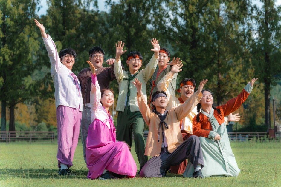 한복과 개량 의상을 입은 출연자들이 잔디밭에서 팔을 들고 웃는 단체 사진