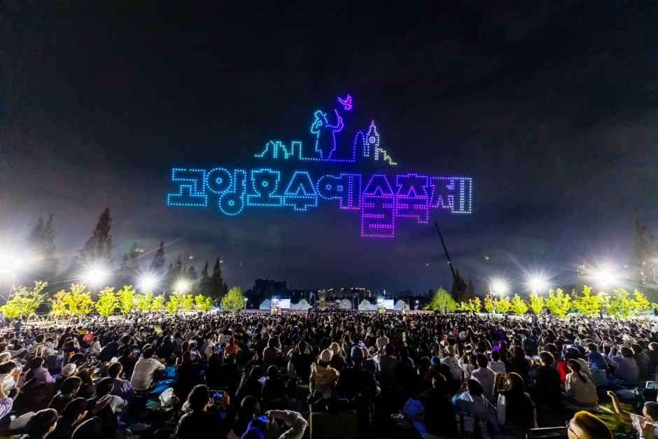 야간 하늘에 드론이 만든 축제 이름 글자와 인물 형상 조명, 그 아래 모인 관람객들