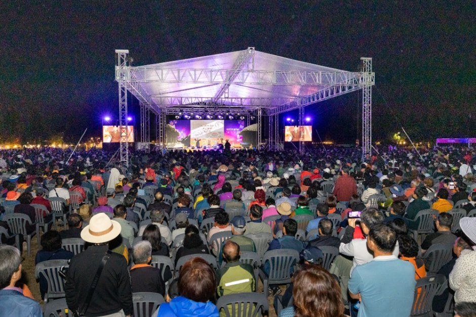 밝은 조명이 비추는 야외 무대 앞에 관객이 의자에 앉아 공연을 보는 구포나루 축제