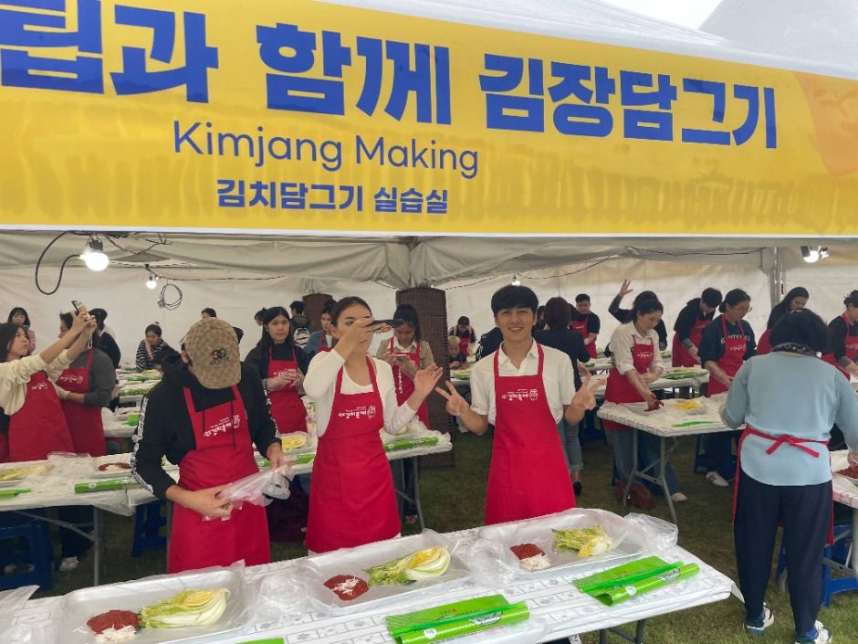 빨간 앞치마를 두른 방문객들이 배추와 양념이 놓인 테이블에서 김장 담그기 체험을 하는 모습