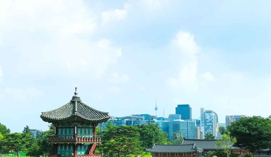 연못 가장자리에 선 경복궁 경회루와 주변 도심 풍경