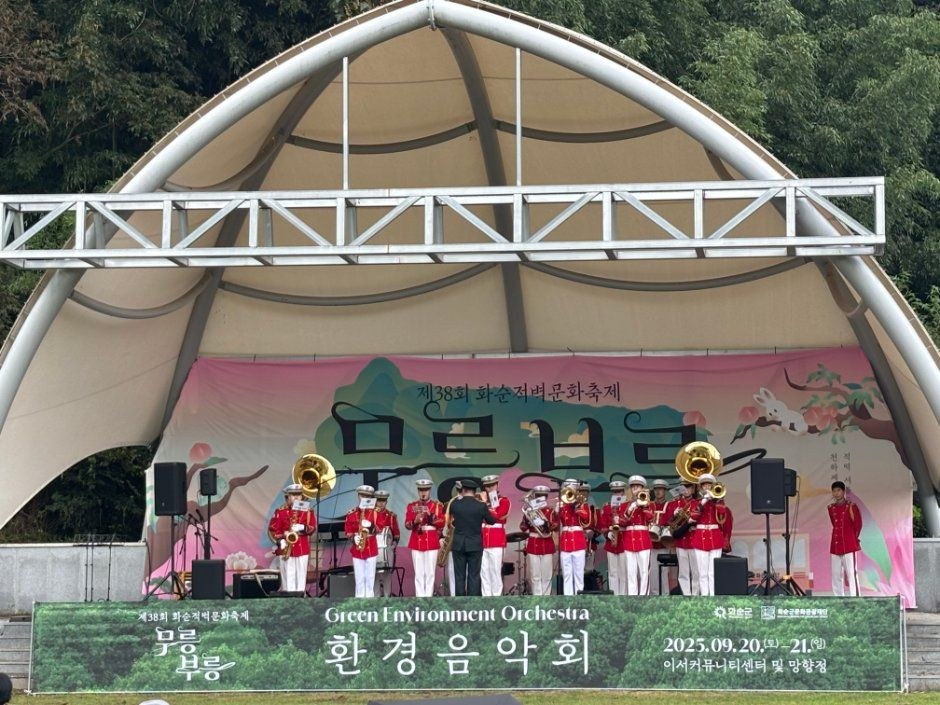 반원형 지붕 무대 위에서 붉은 제복의 악단이 환경음악회를 열고 있는 모습