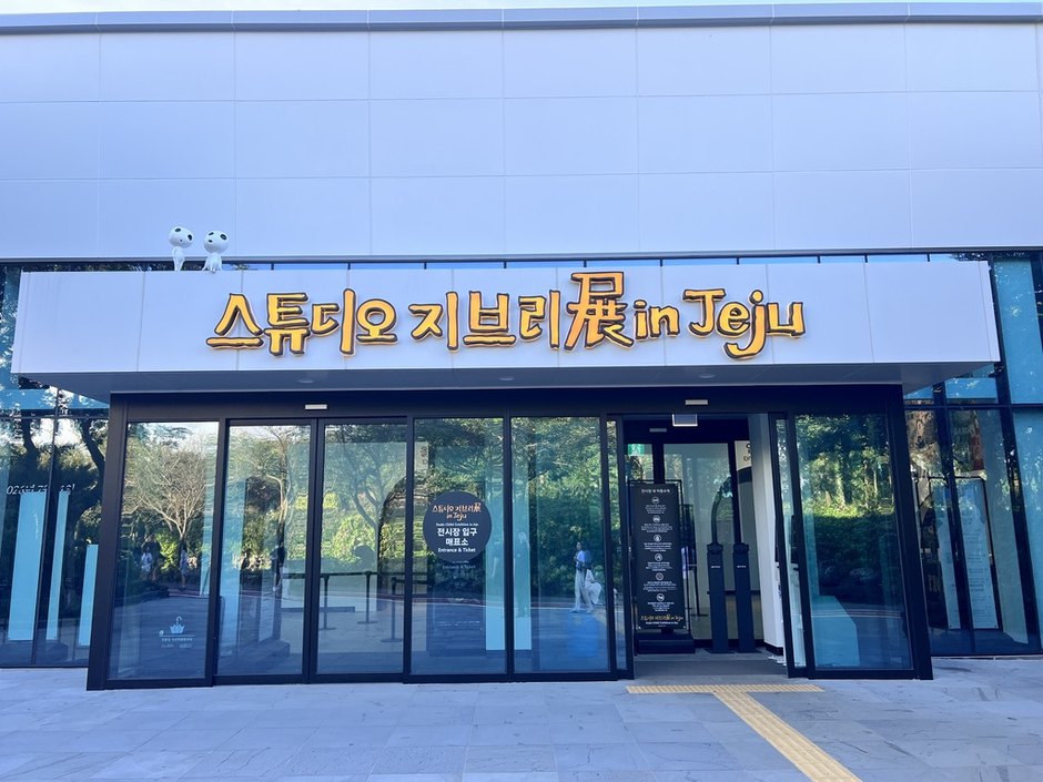 지붕 위에 하얀 숲의 정령 조형물이 앉아 있고 노란 글씨 간판이 붙은 스튜디오 지브리展 in Jeju 입구