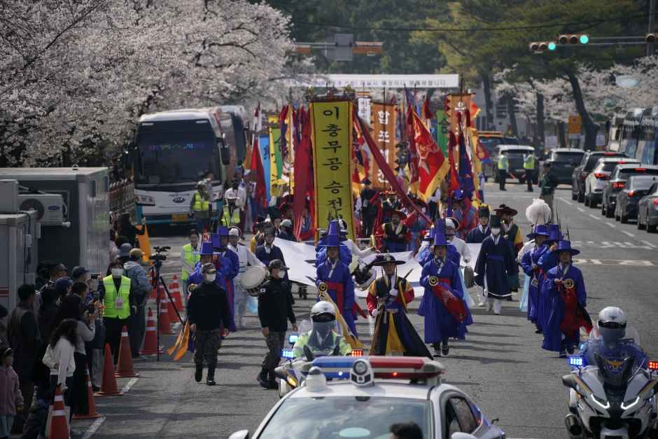 갑옷과 깃발을 든 전통 복장 행렬이 벚꽃 핀 도로를 따라 이충무공 승전행차를 재현하는 모습