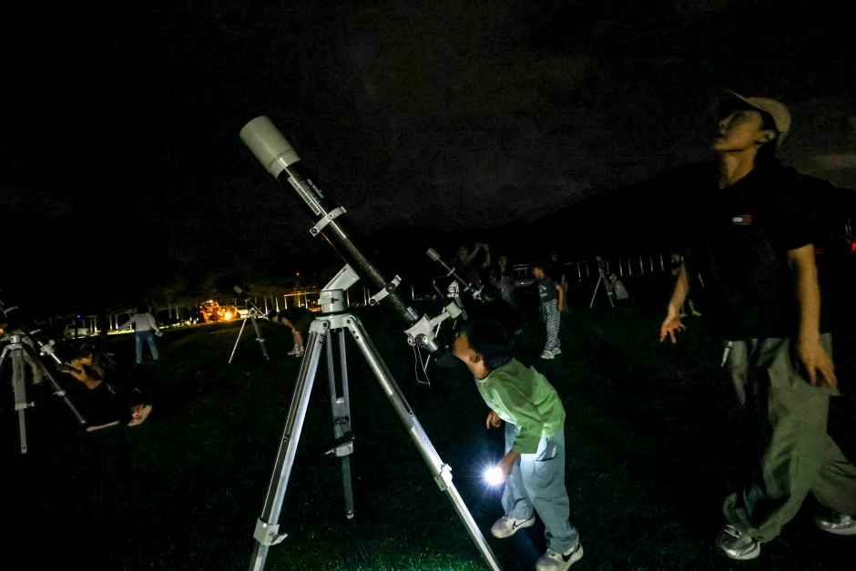 어두운 잔디밭에서 천체 망원경으로 밤하늘을 관찰하는 가족