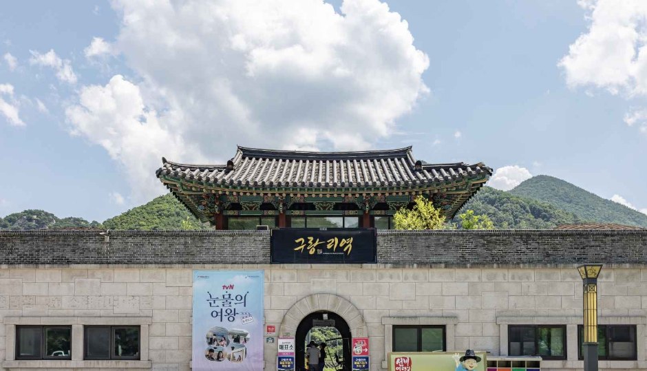 돌담 위에 기와 문루가 있는 문경 철로자전거 입구 건물과 앞을 걷는 사람들