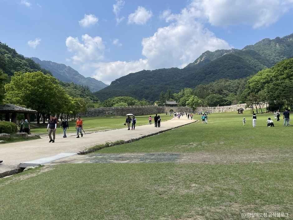 푸른 산 아래 잔디밭과 산책로를 방문객들이 걷고 있는 문경새재 일대