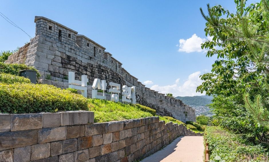 낙산공원 표지와 한양도성 성벽 사이로 이어지는 오르막 산책로