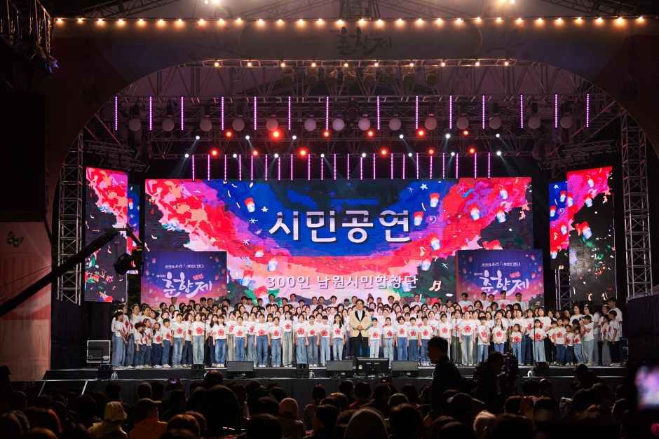 화려한 전통 문양 의상과 부채를 든 공연자들이 야외에서 손을 흔들며 춤을 추는 개막 퍼레이드 장면
