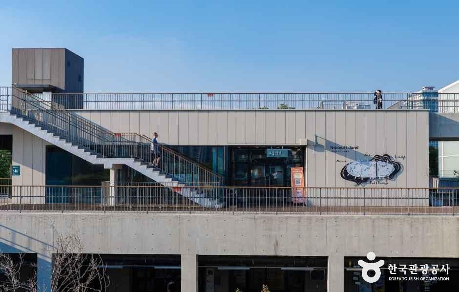 계단형 옥상 산책로와 통유리창 건물, 한 사람이 옥상을 걷고 있는 노들섬 시설 외관