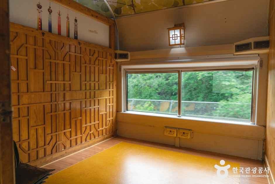 한옥 창살 문양의 나무 벽면과 온돌 느낌의 바닥, 창밖으로 초록 풍경이 보이는 열차 특실 내부