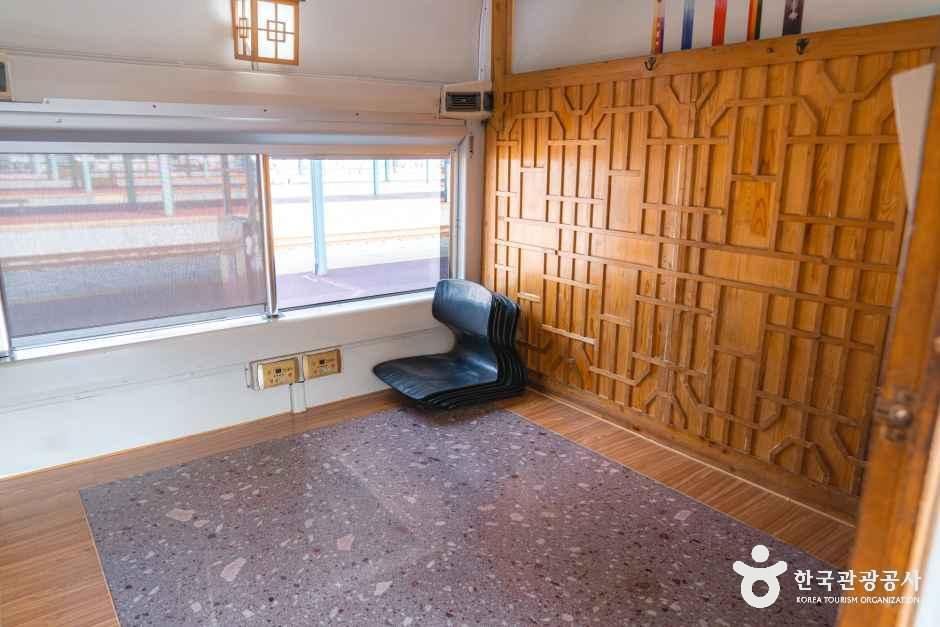 한옥 창살 문양 나무 벽면 앞에 좌식 의자와 방석이 놓인 열차 특실 내부, 창밖으로 역 플랫폼이 보이는 모습