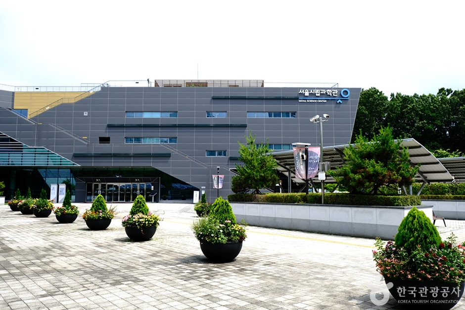 푸른 나무와 화분이 놓인 광장 너머로 보이는 서울시립과학관 건물 외관