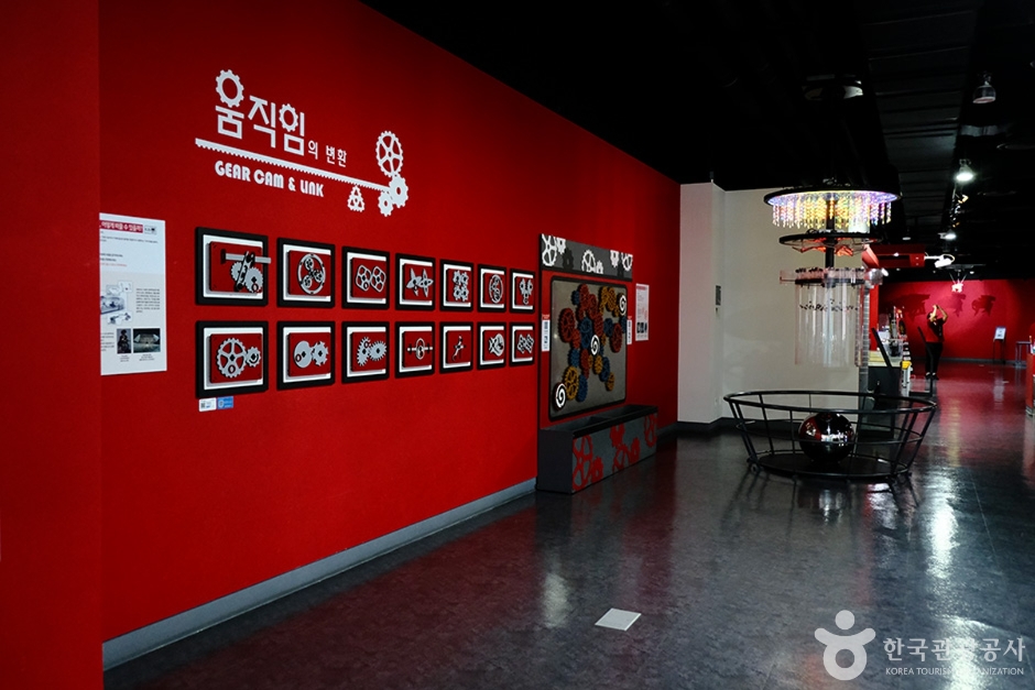 기어와 장치 모형이 붉은 벽면에 전시된 서울시립과학관 공간