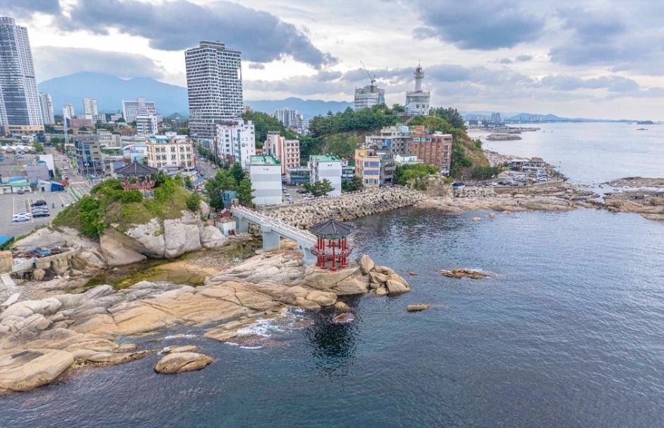바위 위에 붉은 정자가 서 있고 뒤로 속초 시가지와 바다가 보이는 영금정 항공 풍경