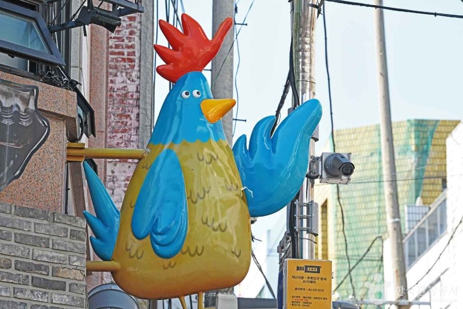 건물 벽에 파란색과 빨간색 닭 조형물이 붙어 있는 수원 통닭거리 골목