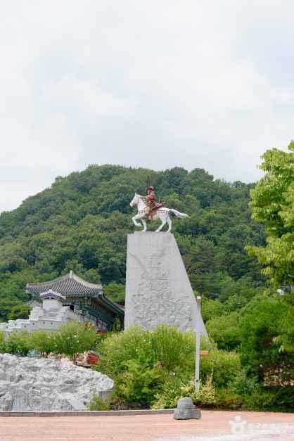 숲이 우거진 언덕 위에 말을 탄 장군 동상이 세워져 있고 그 아래 한옥 건물이 자리한 의령 전경