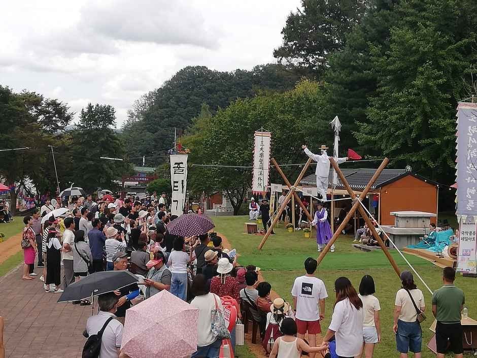 잔디밭에서 관람객들이 우산을 쓰고 서서 무대 공연을 보는 모습