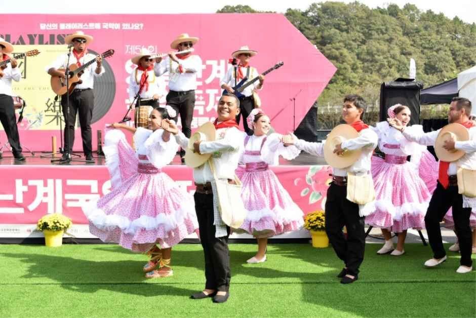분홍 치마와 모자를 쓴 외국 무용단이 잔디밭 무대에서 춤추는 모습