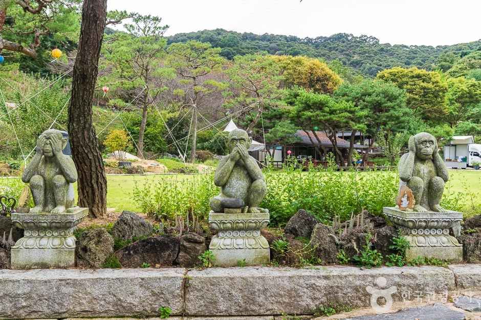 소나무 숲을 배경으로 눈과 입을 가린 세 마리 원숭이 석상이 나란히 놓인 영평사 경내 풍경